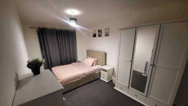 Et soveværelse med seng, natborde, et garderobeskab, en potteplante og en loftlampe.