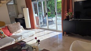 Sala de estar com sofá, mesa de centro, televisão e porta de vidro deslizante para um pátio.