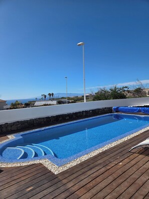 A swimming pool with a wooden deck, surrounded by a stone wall, and a clear view of the ocean and mountains in the background. - Villa Petit Paradis - A little bit of heaven (Callao Salvaje)