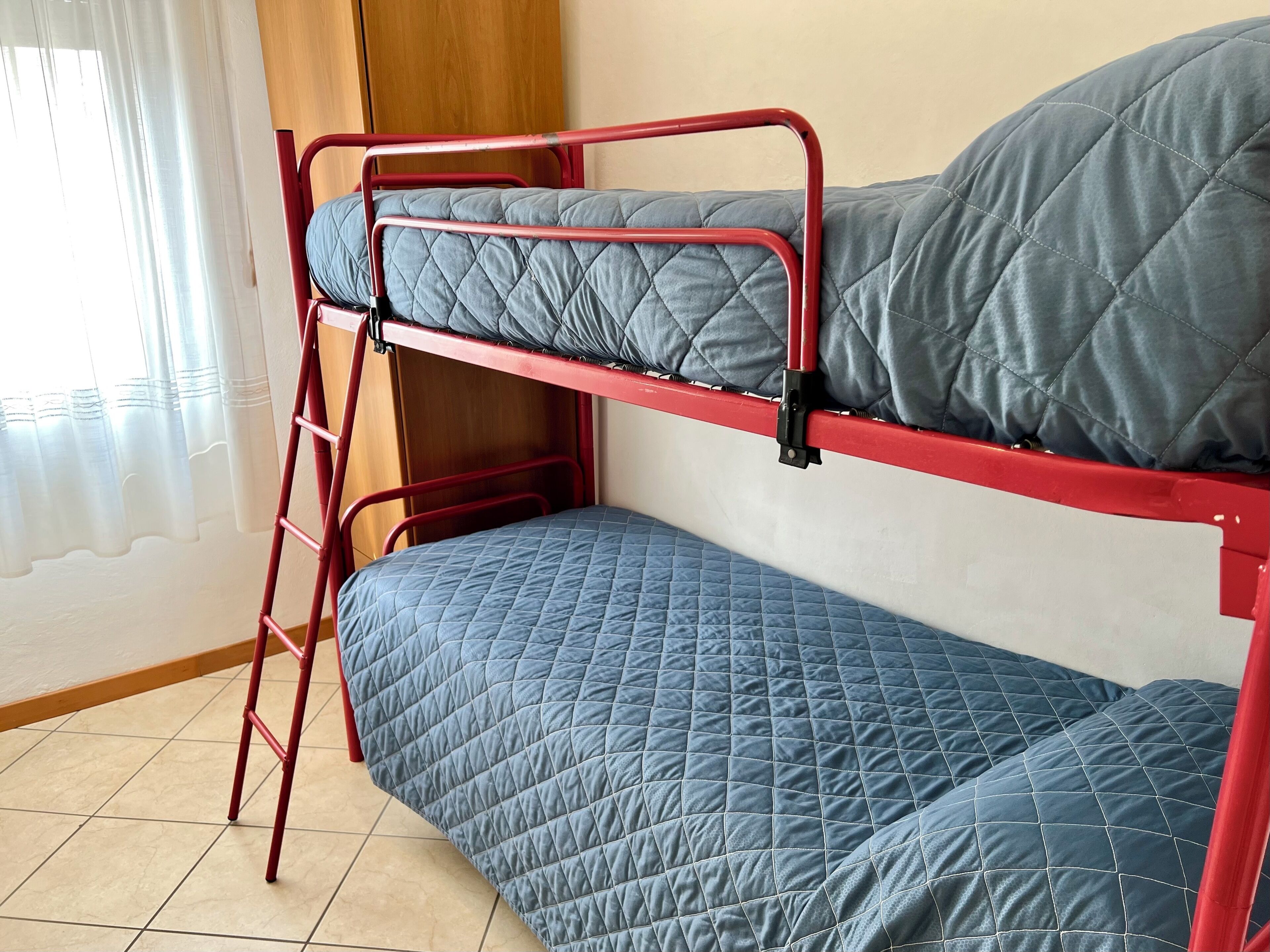 Un letto a castello con una scala, una finestra con tende e un pavimento piastrellato.