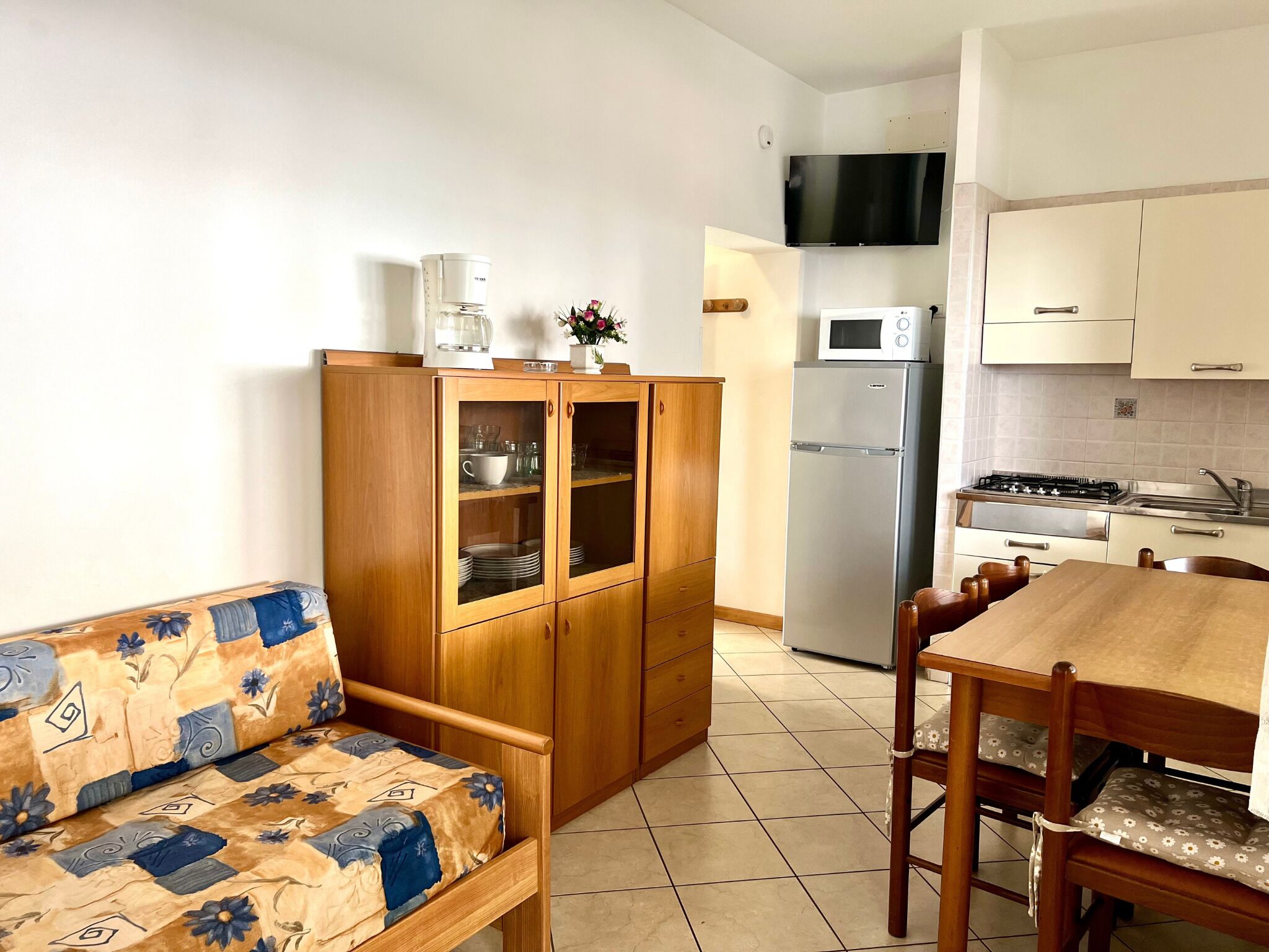 A compact kitchen with a sofa, wooden cabinets, a refrigerator, a microwave, and a stove.
