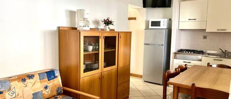 A compact kitchen with a sofa, wooden cabinets, a refrigerator, a microwave, and a stove.