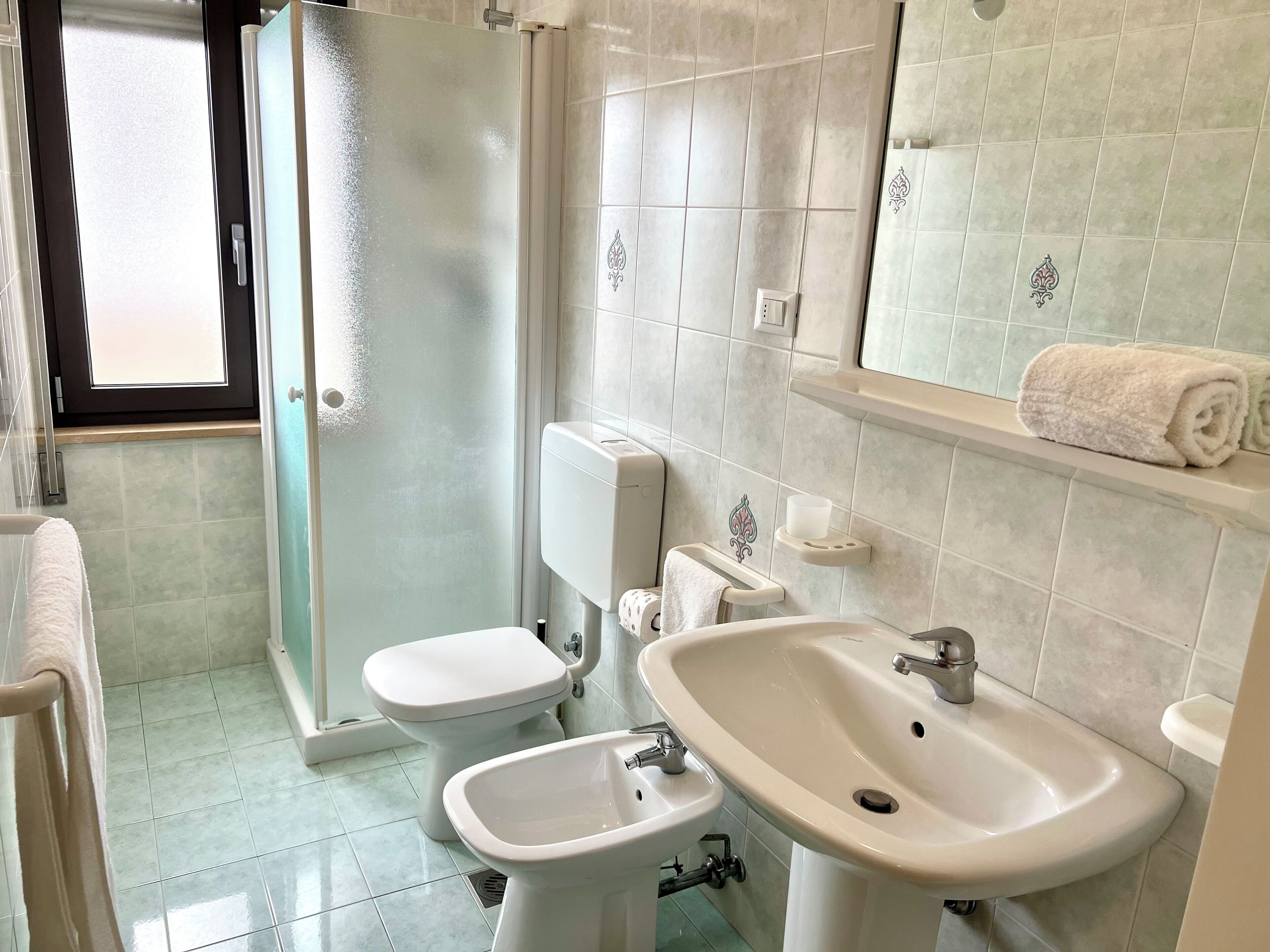 A bathroom with a glass shower enclosure, a toilet, a bidet, a sink, and a towel rack.