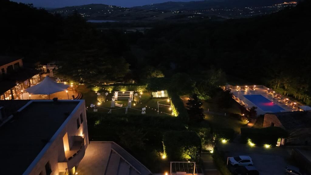 Une vue nocturne d’un complexe hôtelier avec des allées illuminées, une piscine et une végétation luxuriante.