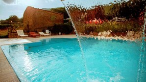 Ein Schwimmbecken mit klarem Wasser, einer Wasserfallanlage und Liegestühlen.
