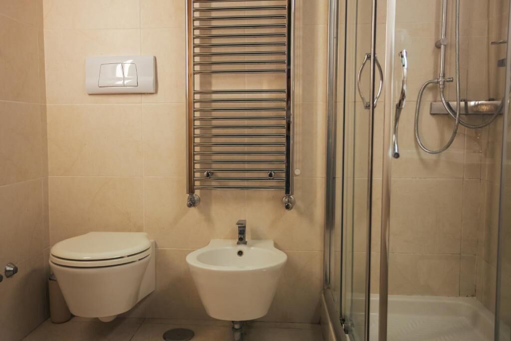 Une salle de bain équipée de toilettes, d’un lavabo, d’un porte-serviettes, d’une douche et d’un interrupteur.