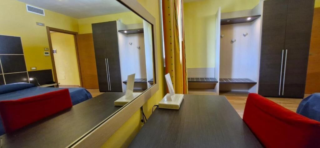 Habitación de hotel con cama, escritorio, espejo, armario y zona de ducha.