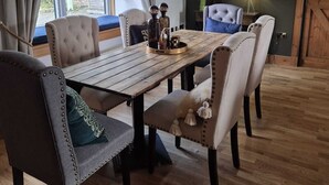 A dining area with a wooden table, upholstered chairs, and a view through a window. - Fabulous 4-bedroom 2.5 bathroom cottage in charming Paisley / Glasgow (Paisley)