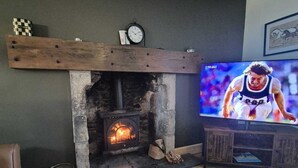 A living room with a stone fireplace, a television, and a clock on the wall. - Fabulous 4-bedroom 2.5 bathroom cottage in charming Paisley / Glasgow (Paisley)