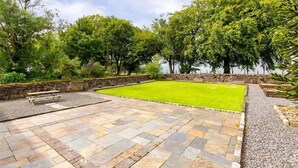 A rectangular lawn with a stone patio in the foreground, surrounded by trees and a stone wall. - Fabulous 4-bedroom 2.5 bathroom cottage in charming Paisley / Glasgow (Paisley)