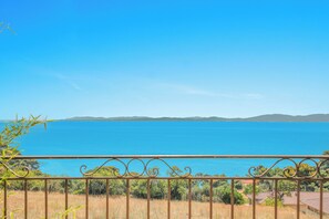 Une vue sur la côte, avec une rambarde en métal, une mer d’un bleu limpide et une terre lointaine à l’horizon.