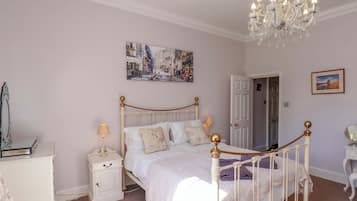 A bedroom with a white bed, a nightstand, a dresser, a chandelier, and a door.