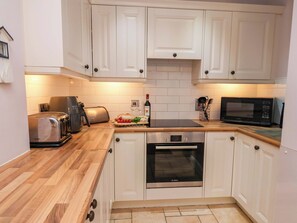 Een moderne keuken met witte kastjes, een Bosch oven, een broodrooster, een magnetron, en een snijplank met brood en tomaten.