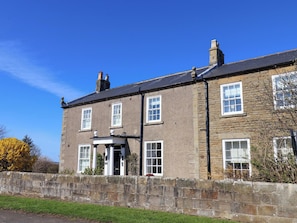 A two-story stone building with a traditional facade, a stone wall in front, and a clear blue sky. - Annie's Place (Whitby)