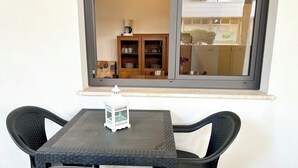 Ein kleiner Tisch mit zwei Stühlen, ein weißer Laternenleuchter und ein Fenster mit Blick auf einen Balkon, der eine Kommode und eine Pflanze zeigt.