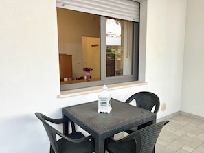 Ein kleiner Tisch im Freien mit Stühlen, ein Fenster mit Blick auf ein Gebäude und ein weißer Laternenleuchter auf dem Tisch.
