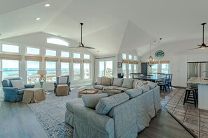 A spacious living room with a large sectional sofa, a dining area, and a kitchen. - Sun Realty pet-friendly 8BR oceanfront home w/ pool & panoramic views! (Nags Head)