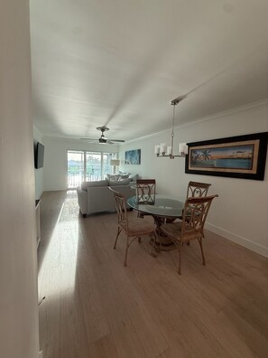 A spacious living area with a dining table, chairs, a ceiling fan, and a view through a glass door. - Fully Furnished Waterfront Condo with Bay Views -Extended Stay Preferred (Apollo Beach)