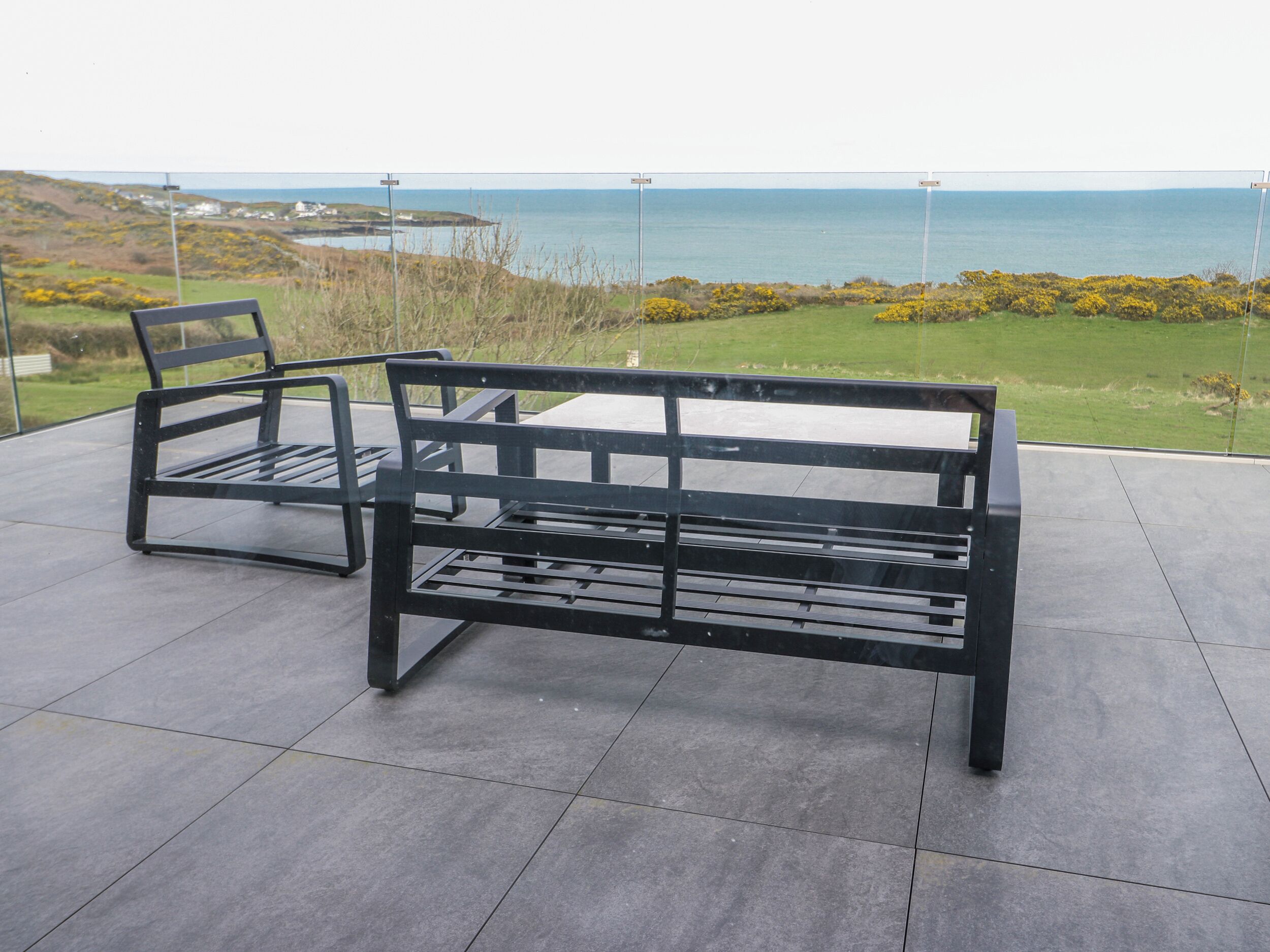 Un banco y una silla en un patio empedrado con vistas al mar y las colinas.