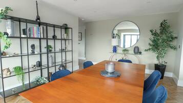 Un comedor con una mesa de madera, sillas azules, una estantería de metal negro y un espejo en la pared.
