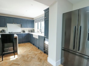 Una cocina moderna con alacenas azul oscuro, un refrigerador de acero inoxidable y un suelo de madera en patrón de espiga.