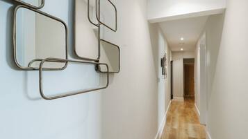 A hallway with a wooden floor, white walls, and a wall-mounted mirror with a geometric metal frame.