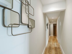 Ein Flur mit Holzboden, weißen Wänden und einem wandmontierten Spiegel mit geometrischem Metallrahmen.