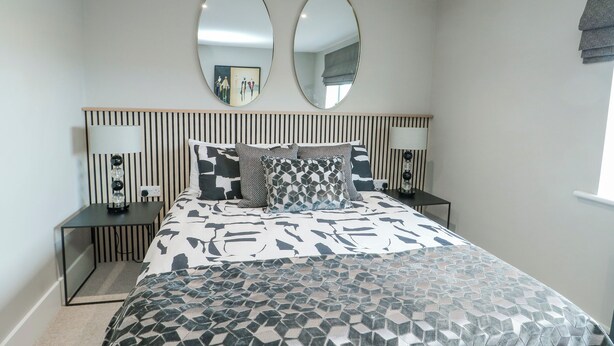 A bedroom with a bed, two bedside tables, two wall mirrors, and a window. - Pengarnedd (Amlwch)