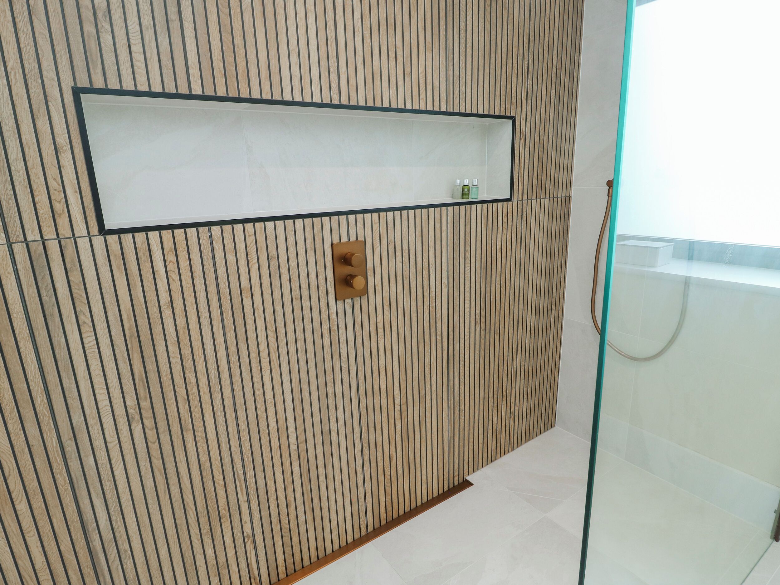 Un baño con pared de paneles de madera, repisas con artículos de aseo y cabina de ducha de vidrio.