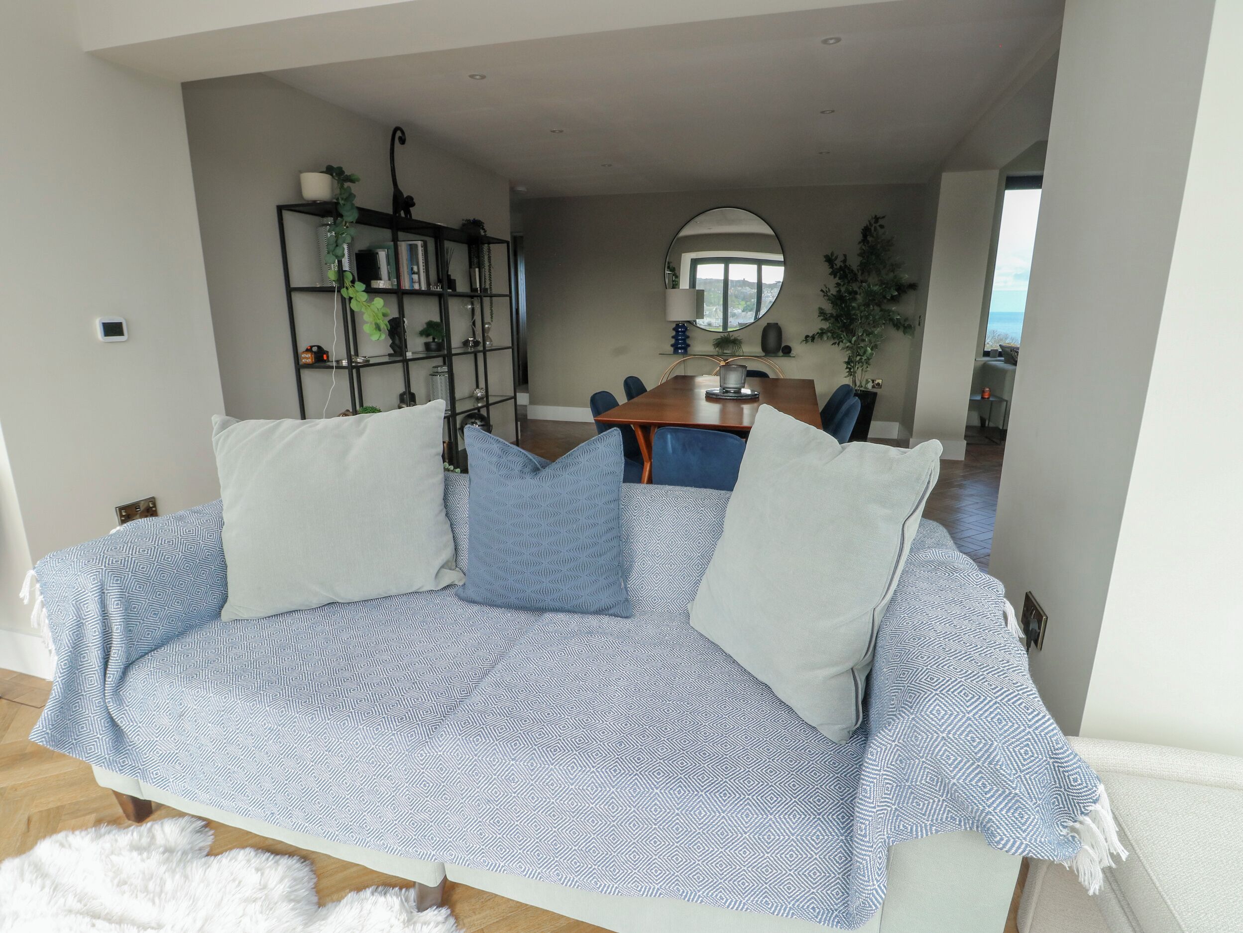 A living room with a patterned sofa, a bookshelf, and a dining area in the background.