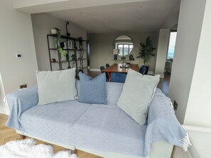 Ein Wohnzimmer mit einem gemusterten Sofa, einem Bücherregal und einem Essbereich im Hintergrund.