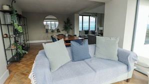 A modern living room with a sofa, a dining area, and a view of the outdoors. - Pengarnedd (Amlwch)