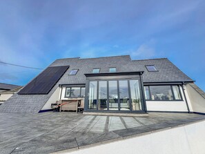 A modern house with a sloped roof, large glass windows, and solar panels. - Pengarnedd (Amlwch)