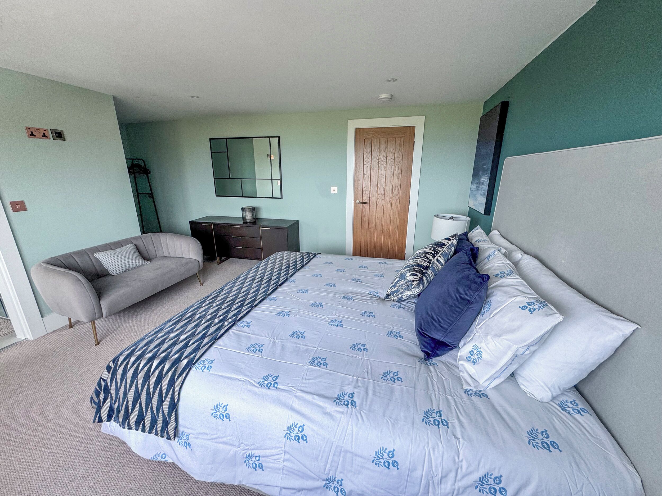 Un dormitorio con cama, sofá, escritorio, espejo y puerta.