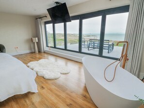 A modern bathroom with a large bathtub, a shower, and a view of the sea through large windows. - Pengarnedd (Amlwch)