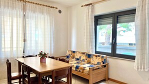 A room with a dining table, chairs, a sofa, a window with curtains, and a view of the outside. - Great Accommodation for Groups in Lignano (Lignano Sabbiadoro)