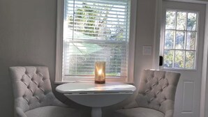 Una habitación con dos sillones tapizados, una mesa blanca y una ventana con persianas.