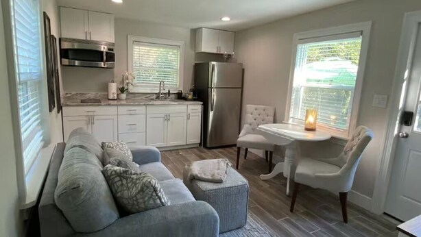 Una cocina compacta con armarios blancos, un refrigerador de acero inoxidable y un comedor con mesa y sillas.