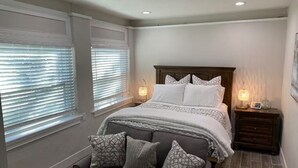 Un dormitorio con cama, lámparas de noche, mesita de noche y ventana con persianas.