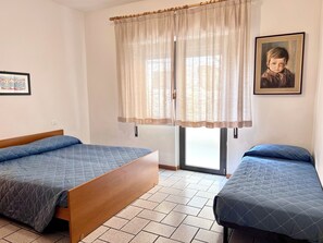 A room with two beds, a window with curtains, a framed picture on the wall, and a tiled floor. - Cozy Flat Perfect for Group Getaways (Lignano Sabbiadoro)