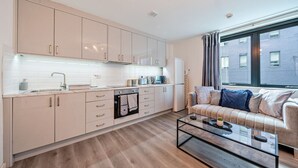 Een moderne keuken met lichte kasten, een ingebouwde oven en een salontafel in de woonkamer.