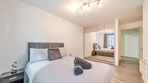Een moderne slaapkamer met een bed, nachtkastje en een grote spiegel die de kamer weerspiegelt.