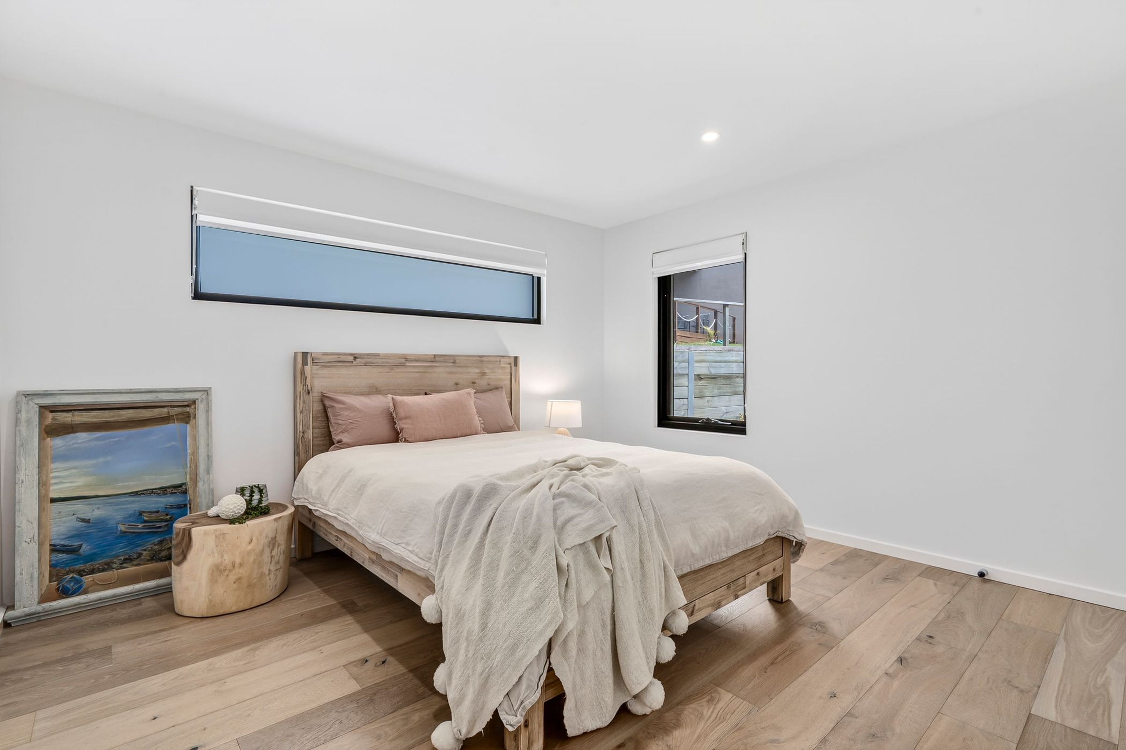 Un dormitorio con una cama de madera, una mesita de noche, una lámpara, un cuadro enmarcado y un ventanal con vistas.