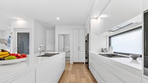 A modern kitchen with white cabinetry, a central island, and a wooden floor. - 9 Oceania (Lorne)