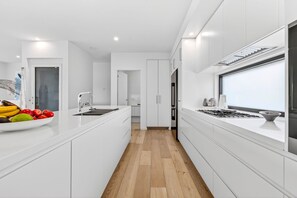 A modern kitchen with white cabinetry, a central island, and a wooden floor. - 9 Oceania (Lorne)