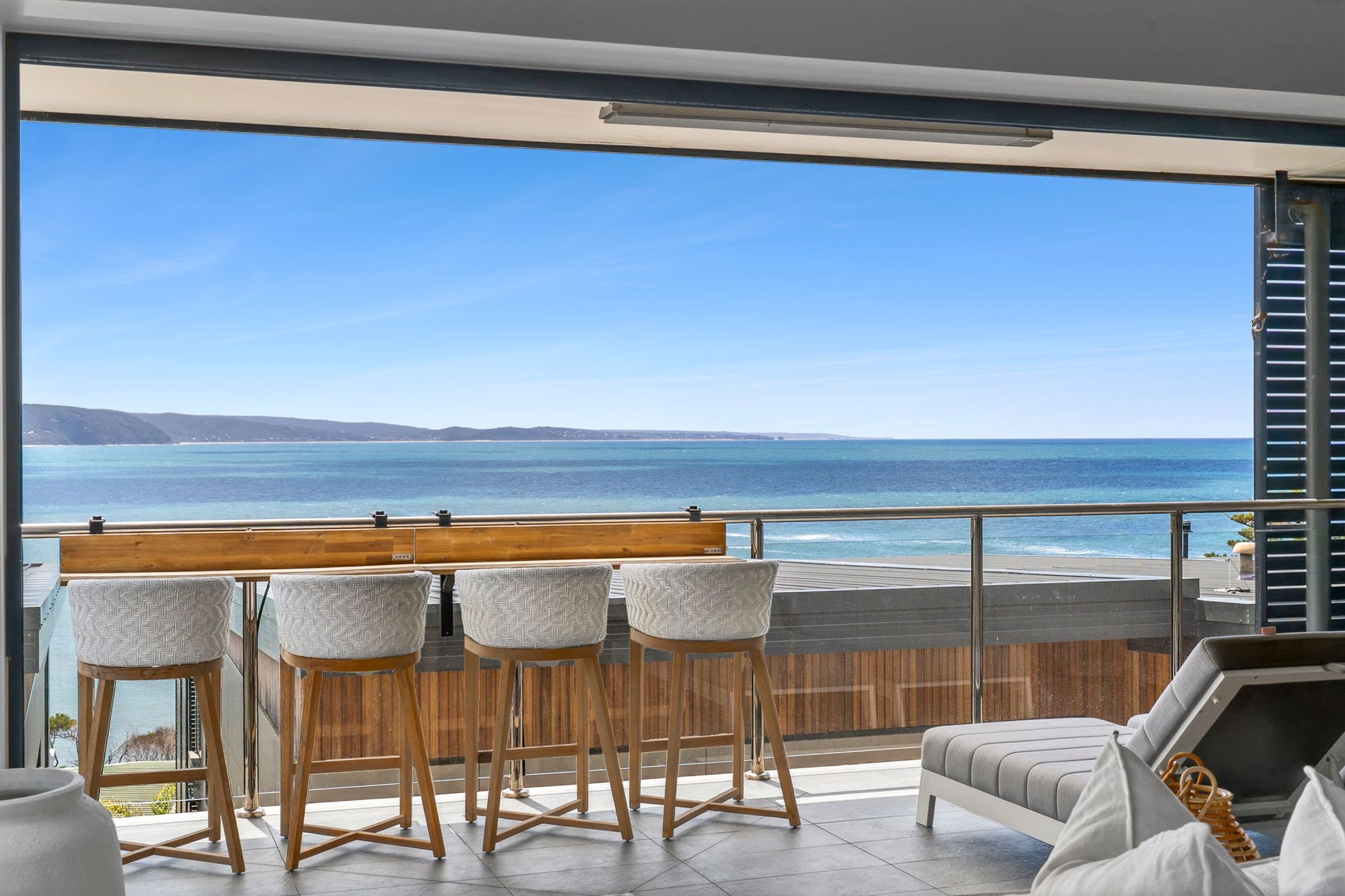 A balcony with a view of the ocean, wooden bar stools, and a sofa.
