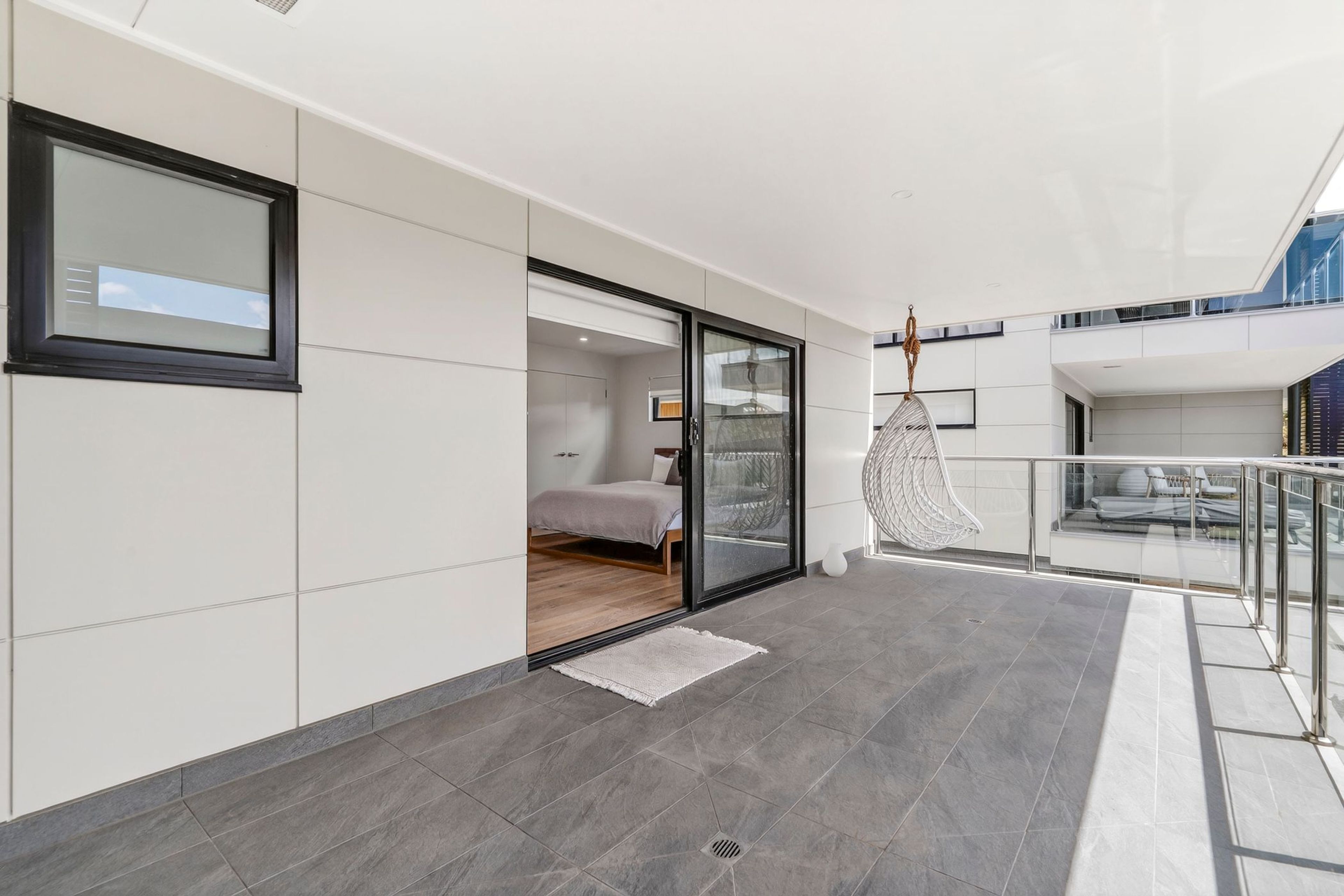 Een modern interieur met een bed, een glazen deur naar een balkon en een hangstoel.