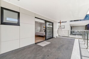 A modern interior with a bed, a glass door leading to a balcony, and a hanging chair. - 9 Oceania (Lorne)