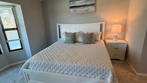 Un dormitorio con cama, mesita de noche, lámpara, ventana con persianas y un cuadro en la pared.