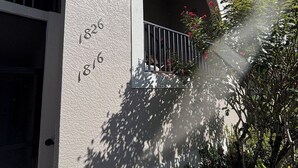 Un edificio con fachada texturizada, un balcón con barandilla de metal y una puerta.